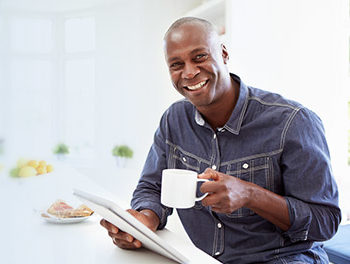 Man with tablet thinking happily and drinking coffee
